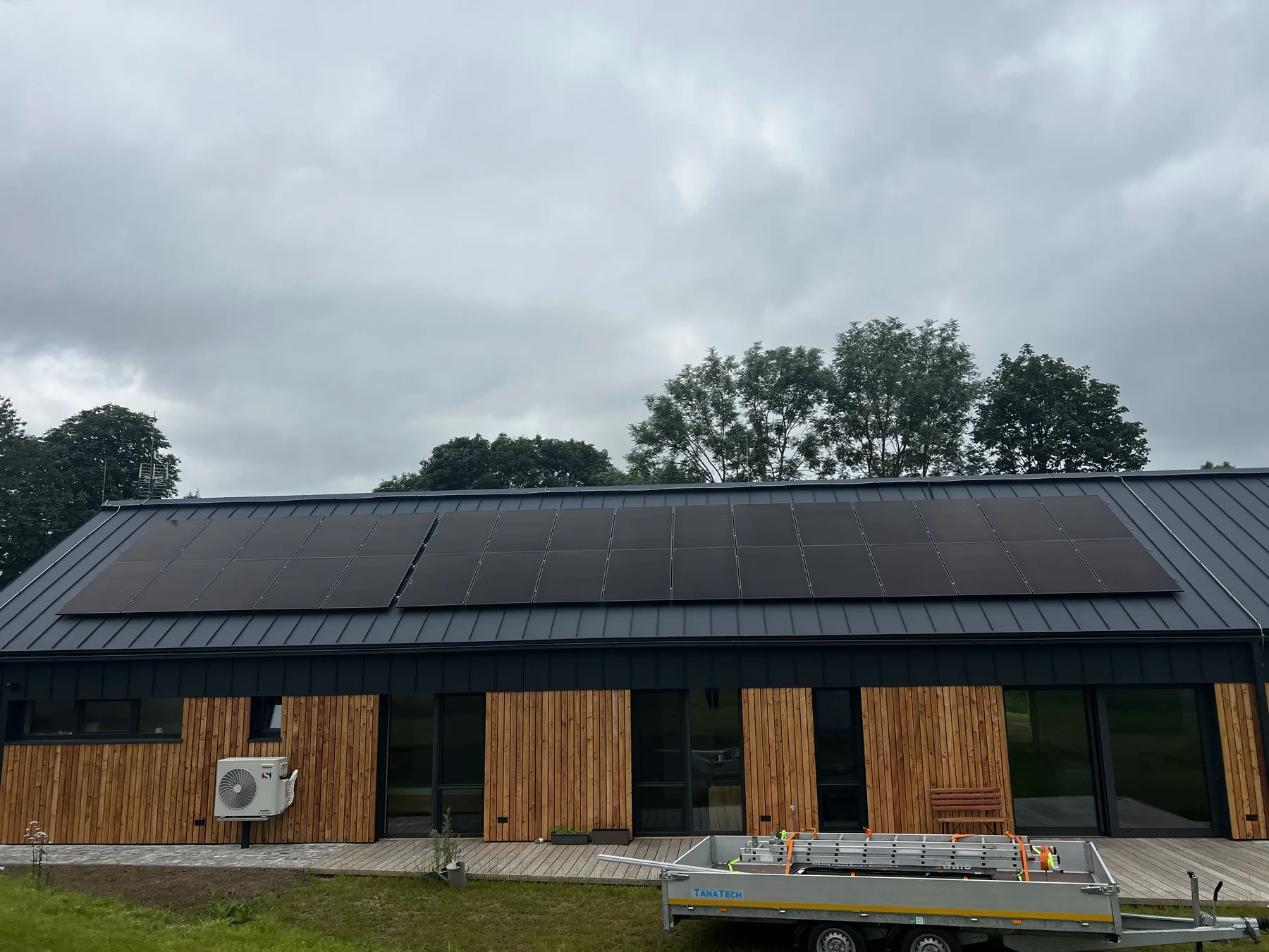 Celkový pohled na fotovoltaické panely osazené na střeše domu s dřevěným obkladem.
