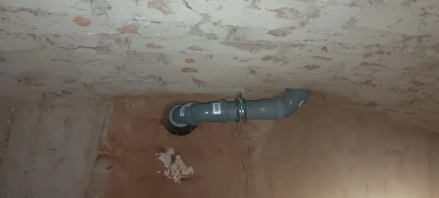 Odpadní potrubí vedené u stěny s navazujícím prostupem. Snímek dokumentuje potrubí, nikoli způsob vytvoření otvoru.